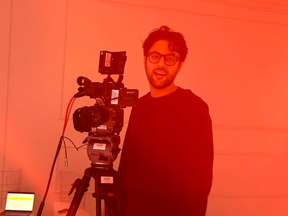 Rishi Kara beside a cinema camera on a red-lit set
